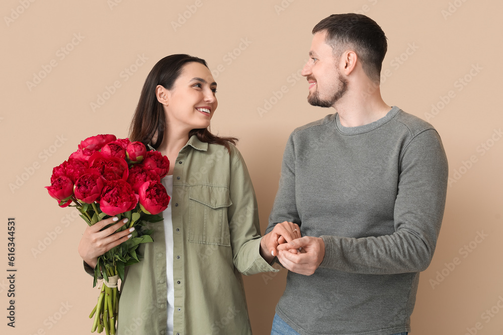 Happy engaged couple with flowers holding hands on beige background