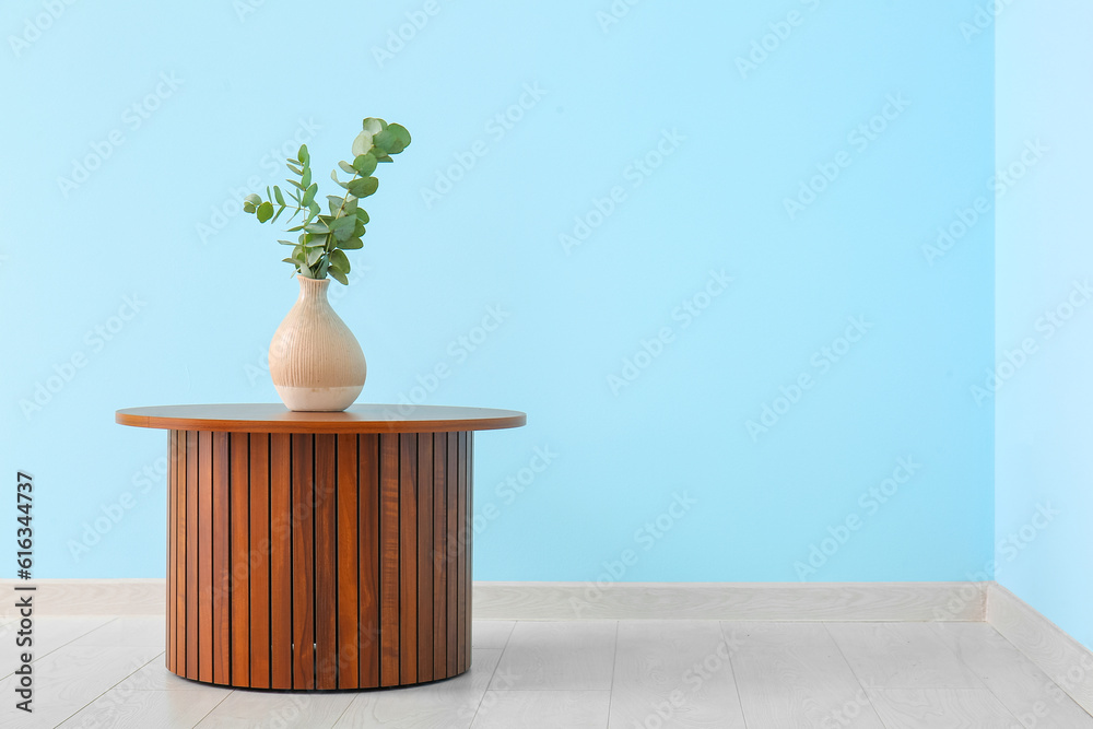 Wooden coffee table with eucalyptus branches in vase near blue wall