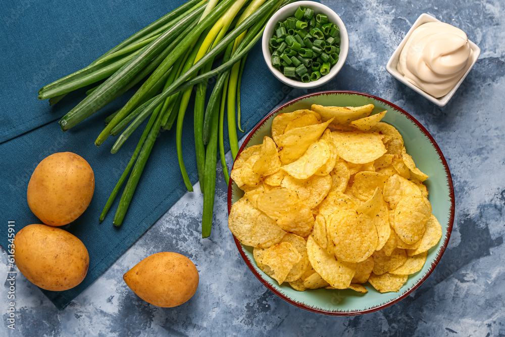 Bowls of tasty sour cream with sliced green onion and potato chips on blue background