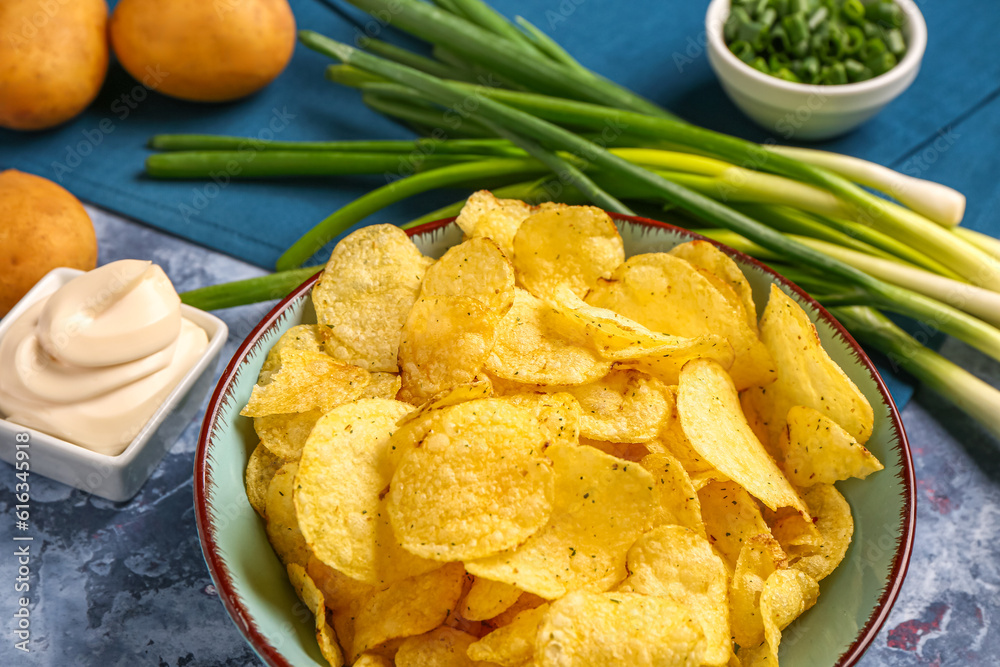 Bowls of tasty sour cream with sliced green onion and potato chips on blue background