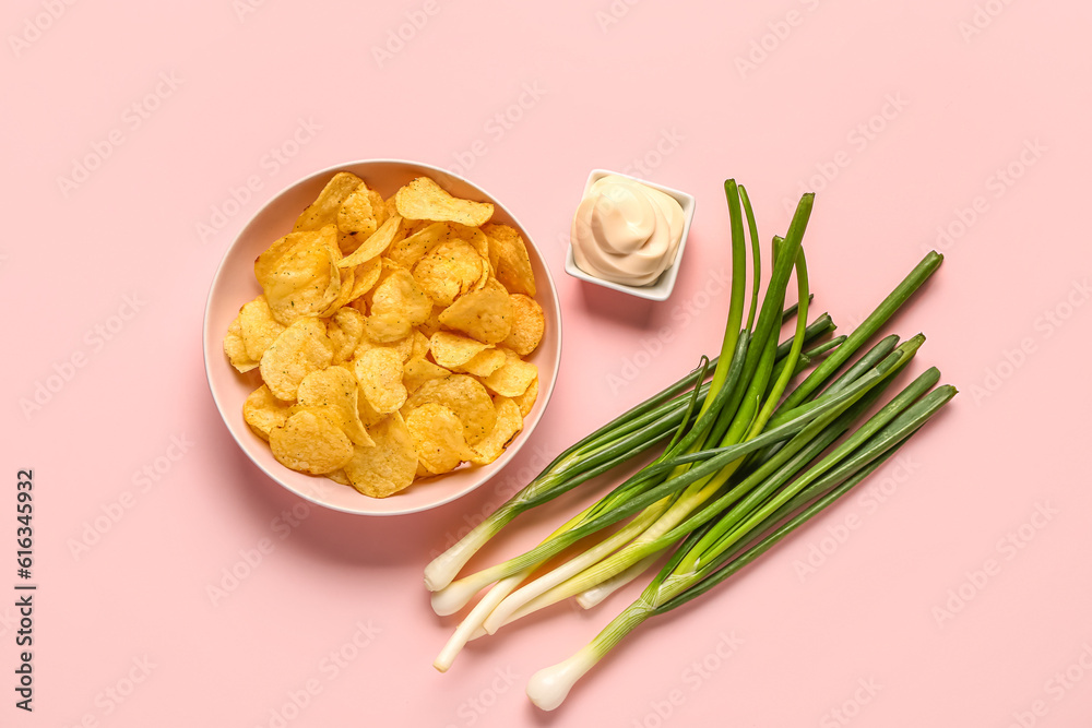 Bowl of tasty sour cream with green onion and potato chips on pink background