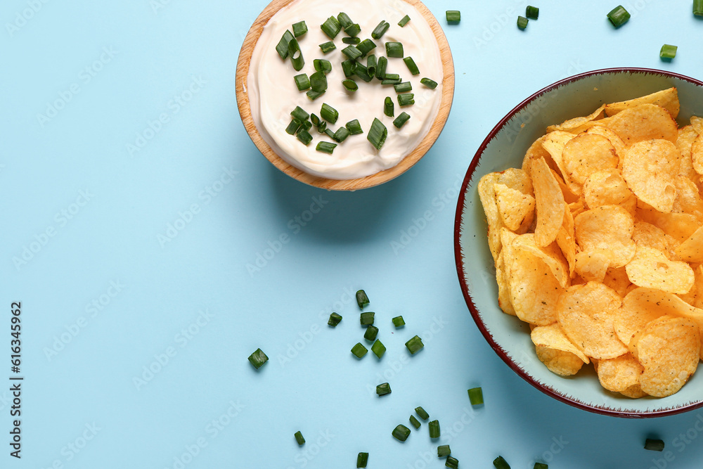 Bowl of tasty sour cream with sliced green onion and potato chips on blue background