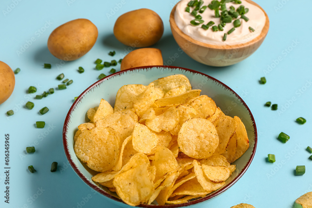 Bowl of tasty sour cream with sliced green onion and potato chips on blue background