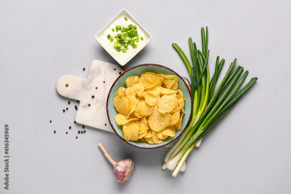 Bowl of tasty sour cream with sliced green onion and potato chips on grey background