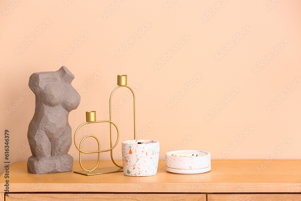 Holders with candles and decor on table near beige wall in room