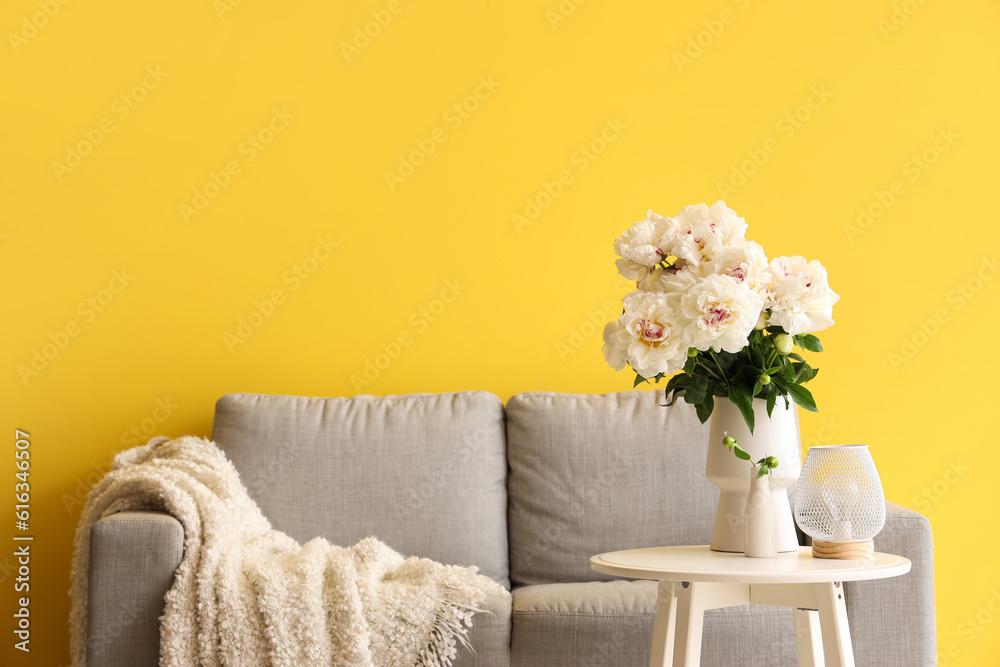 Vase of white peonies with coffee table and couch near yellow wall