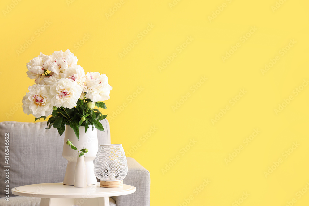 Vase of white peonies with coffee table and couch near yellow wall