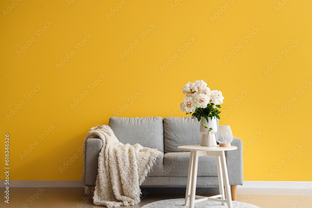 Vase of white peonies with coffee table and couch near yellow wall