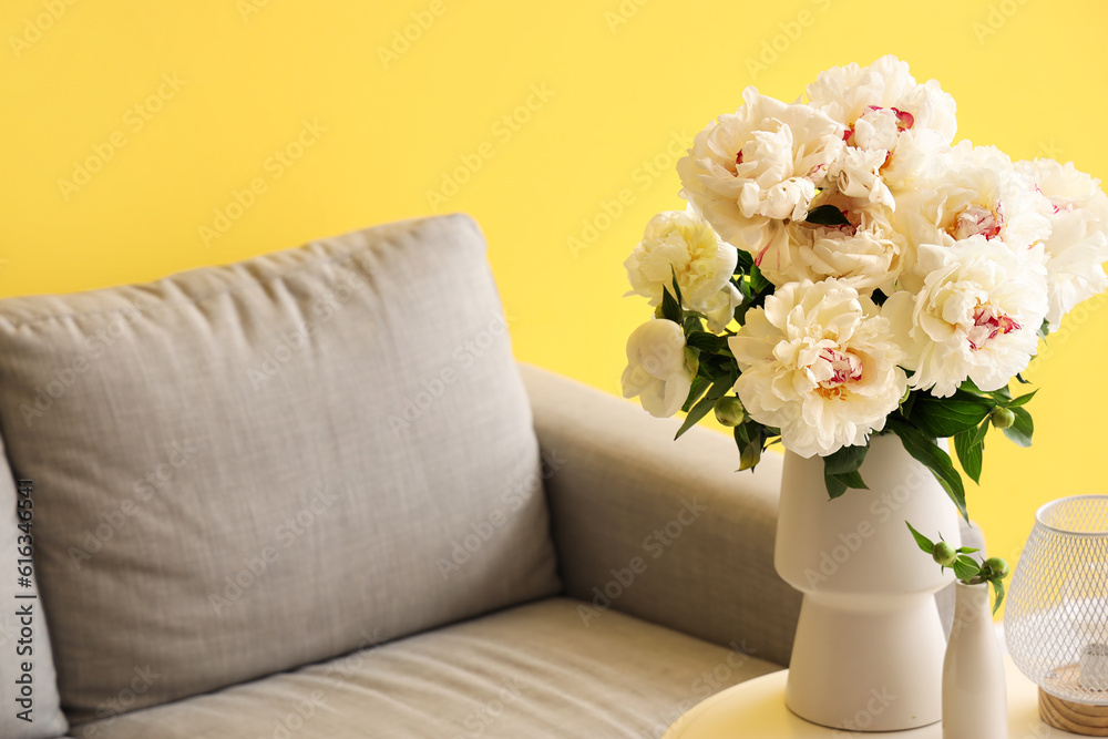 Vase of white peonies with coffee table and couch near yellow wall