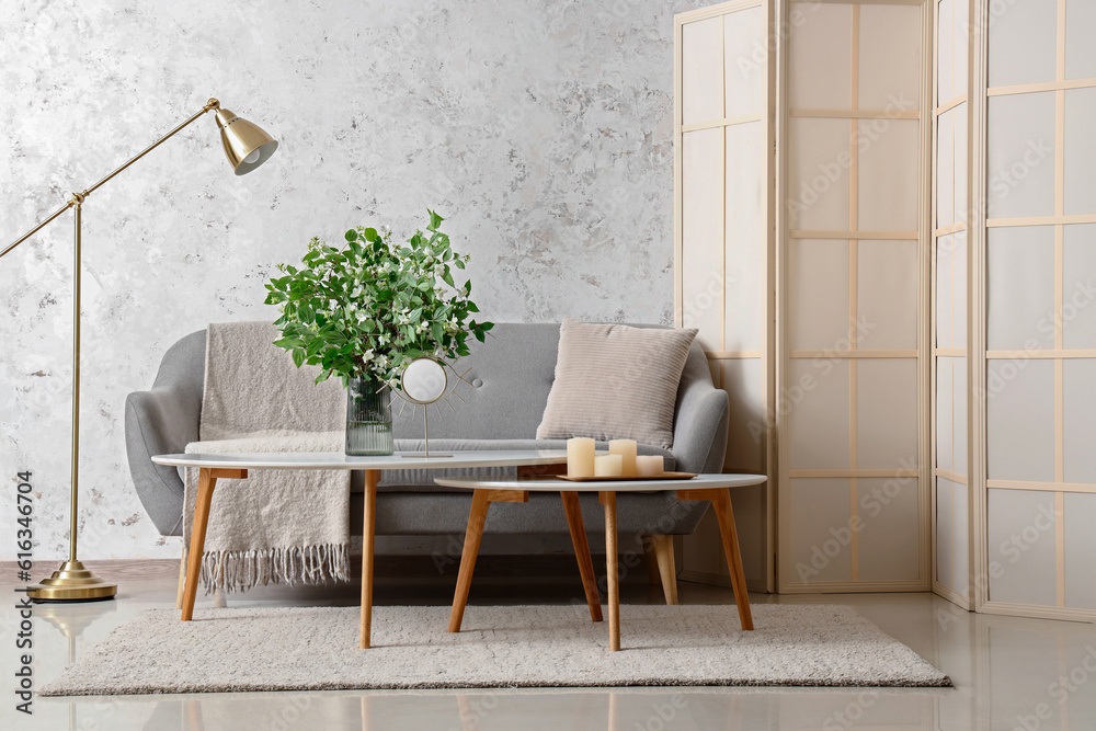 Interior of living room with cozy grey sofa and blooming jasmine flowers on coffee table