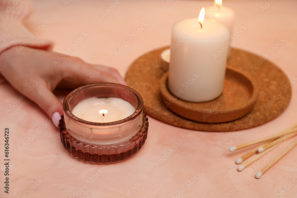 Woman with burning candle on beige background, closeup