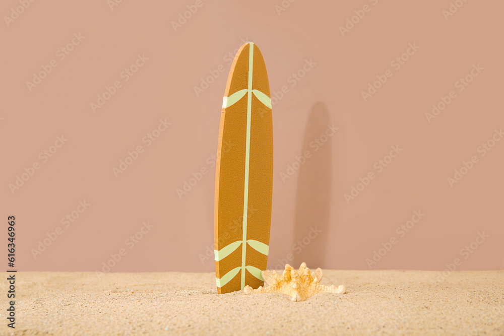 Mini surfboard with starfish on sand against brown background