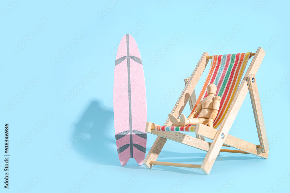 Creative composition with miniature surfboard, deckchair and wooden mannequin on blue background