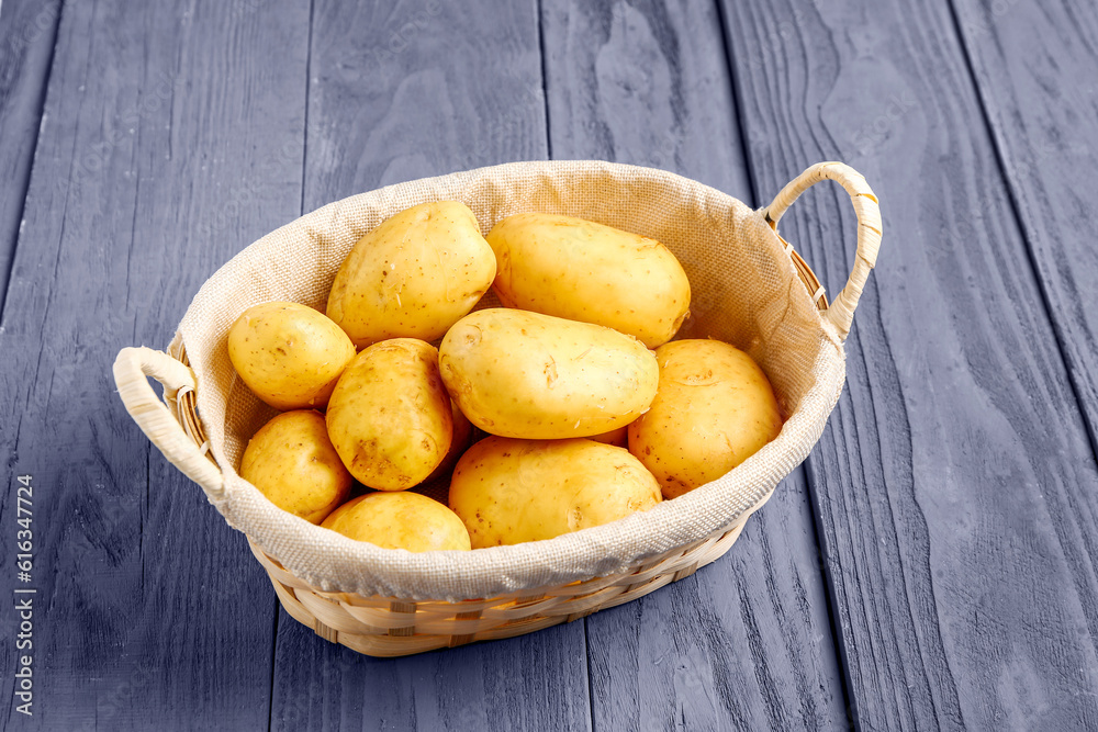 Wicker basket with raw baby potatoes on blue wooden background