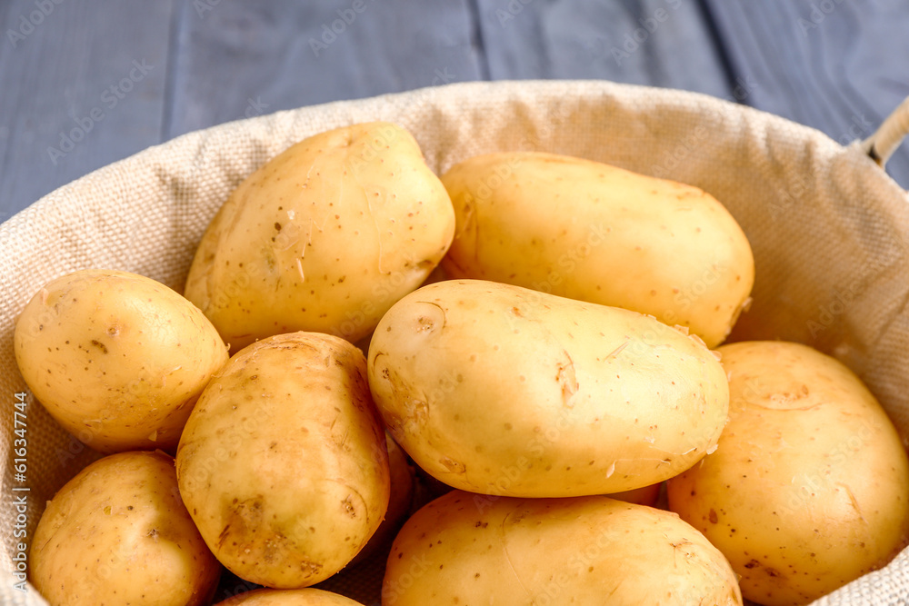 Basket with raw baby potatoes on blue wooden background, closeup