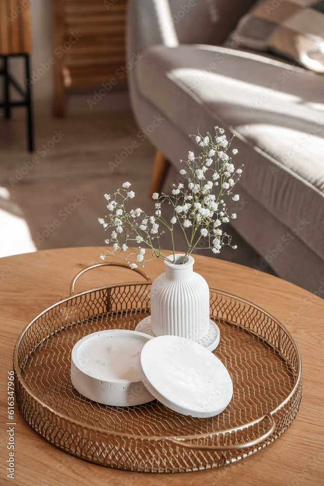 Tray with white candle and gypsophila flowers on table in living room, closeup