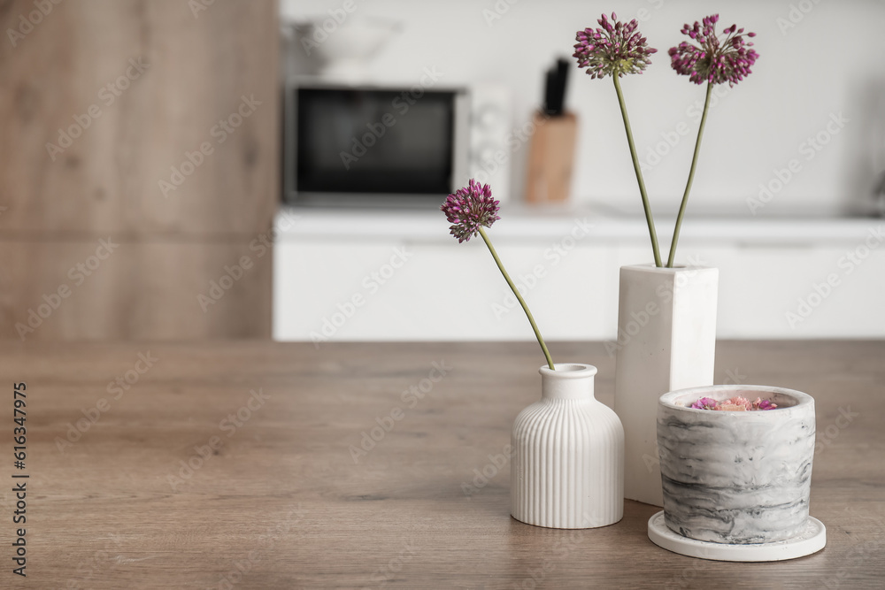 Beautiful flowers and candle on table in light kitchen, closeup