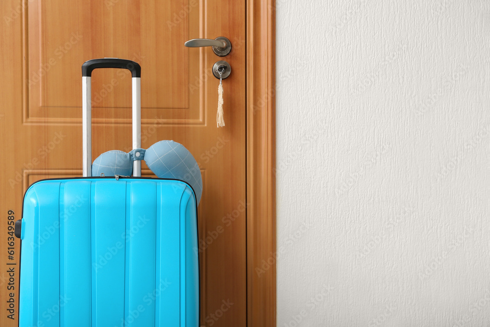 Blue suitcase with travel cushion near door in room. Travel concept