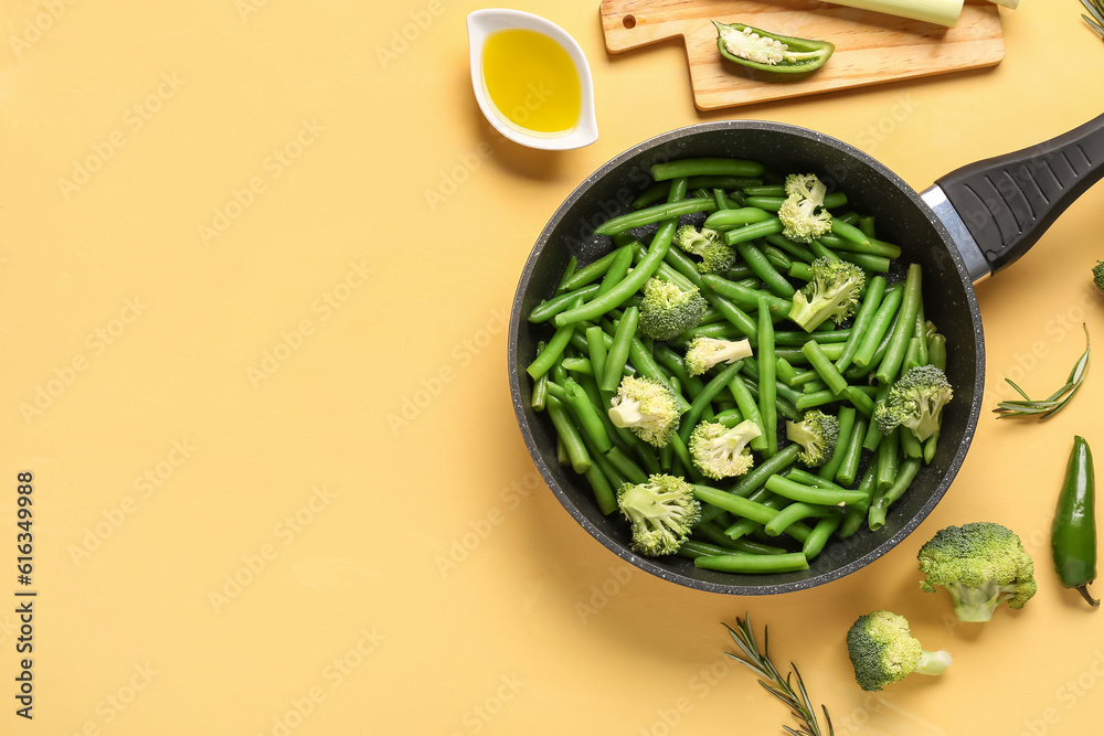 Frying pan with fresh vegetables on yellow background