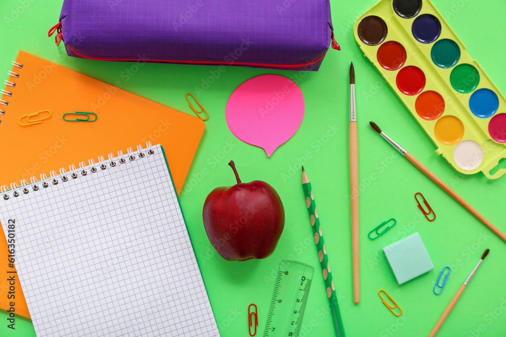 Fresh red apple with different stationery on green background