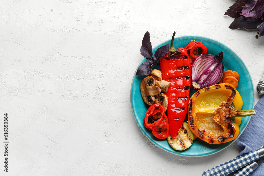 Plate with grilled vegetables and basil on white table