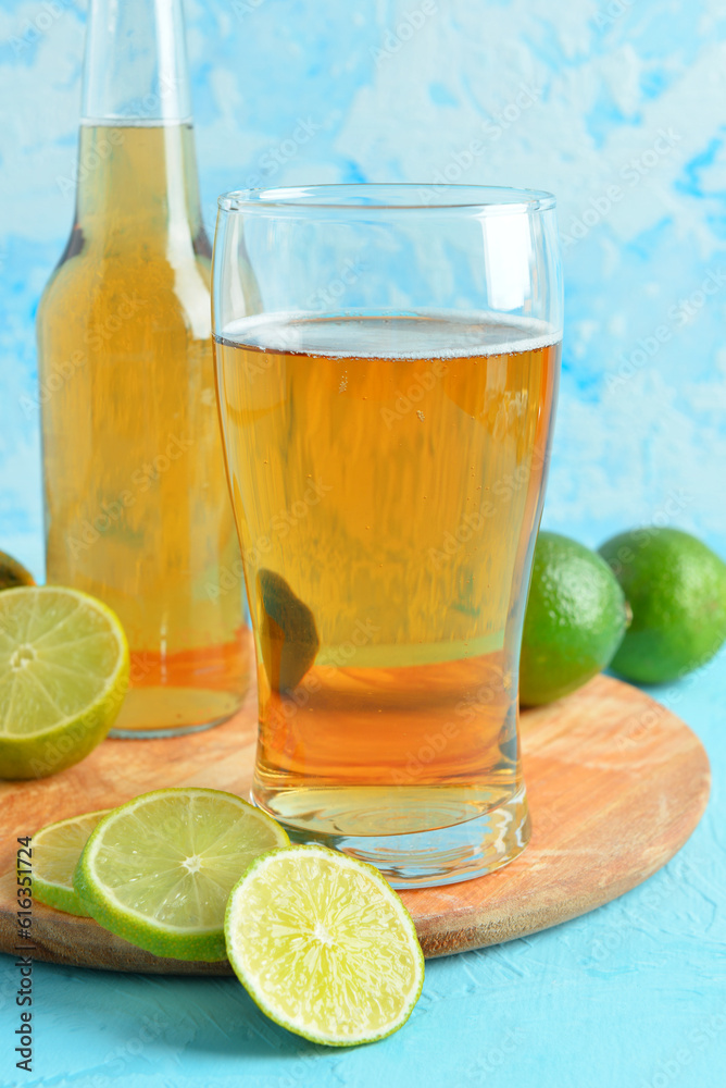 Glass and bottle of cold beer with lime on blue background