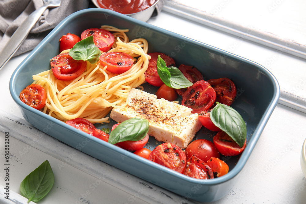 Baking dish of tasty pasta with tomatoes and feta cheese on white wooden background