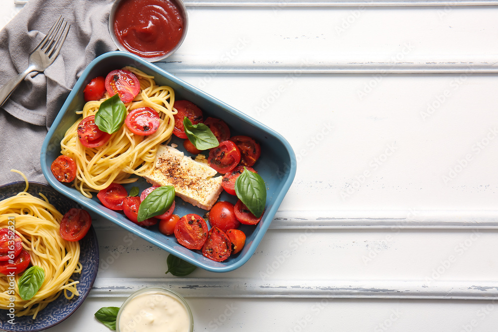 Baking dish of tasty pasta with tomatoes and feta cheese on white wooden background