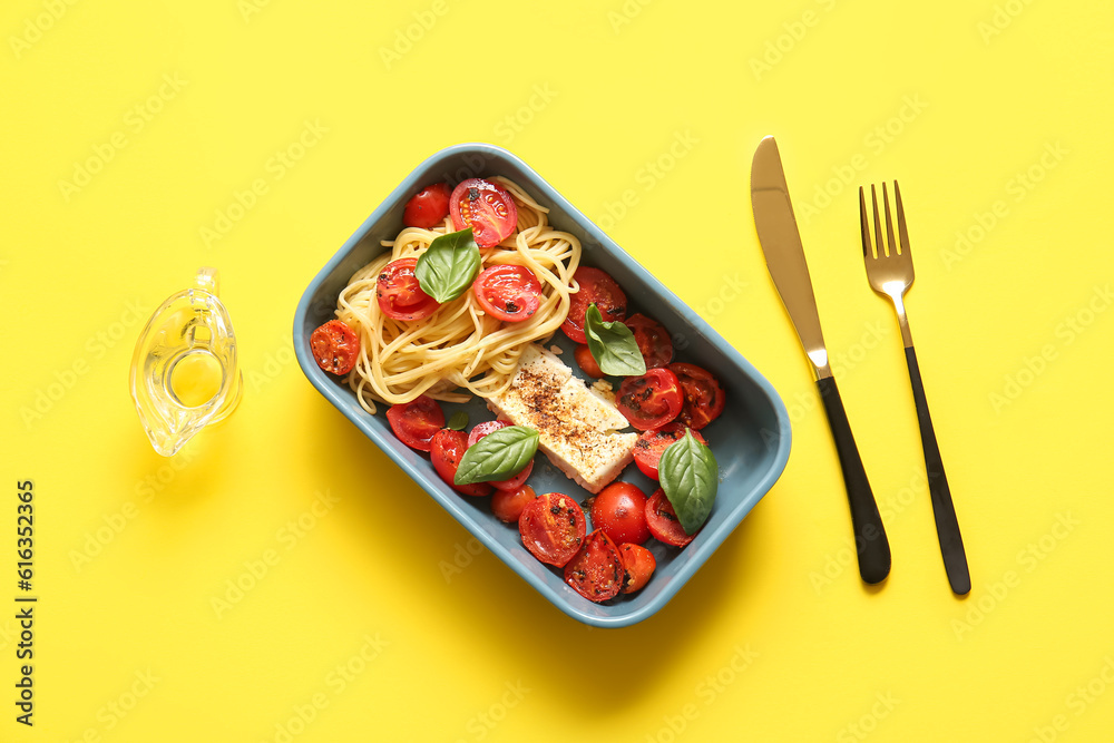 Baking dish of tasty pasta with tomatoes and feta cheese on yellow background