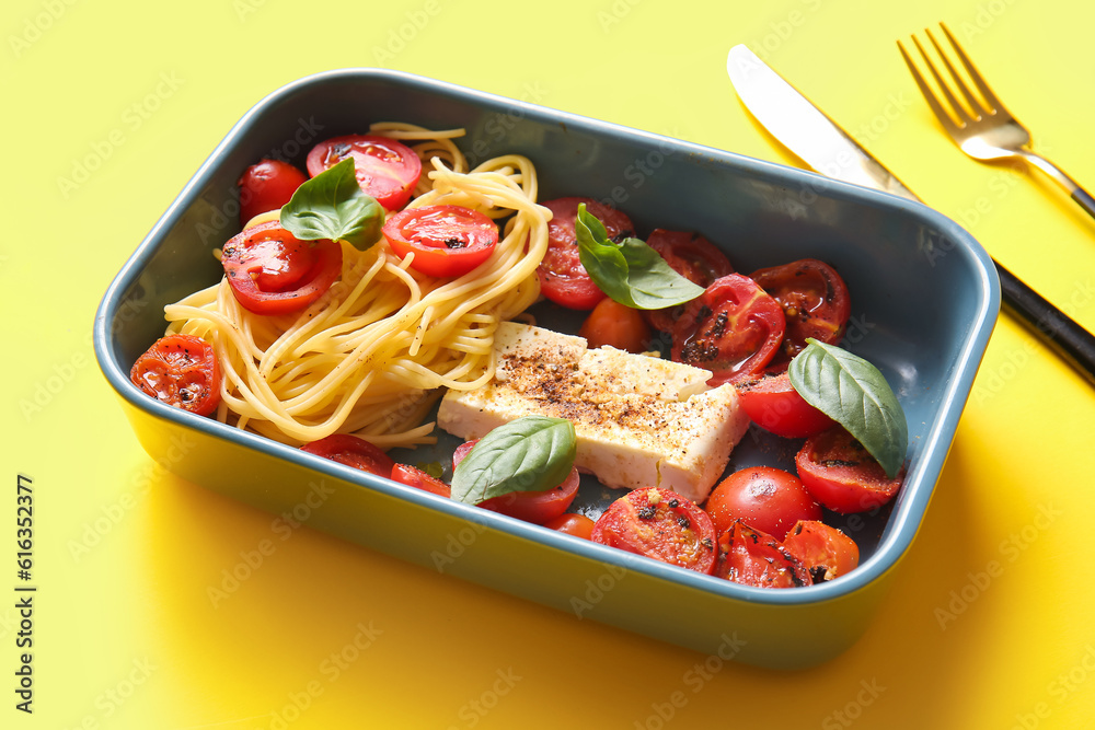 Baking dish of tasty pasta with tomatoes and feta cheese on yellow background