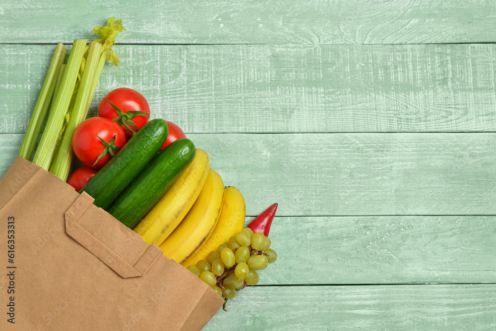 Paper bag with fresh vegetables and fruits on green wooden background