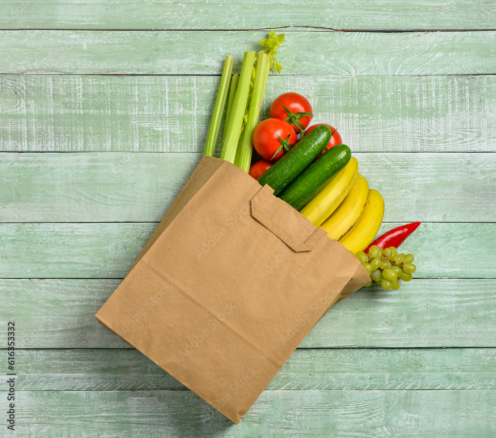 Paper bag with fresh vegetables and fruits on green wooden background