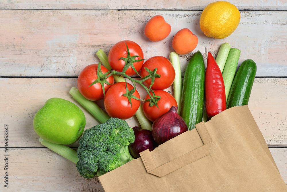 Paper bag with fresh vegetables and fruits on light wooden background