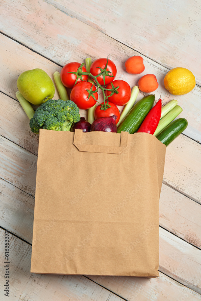 Paper bag with fresh vegetables and fruits on light wooden background