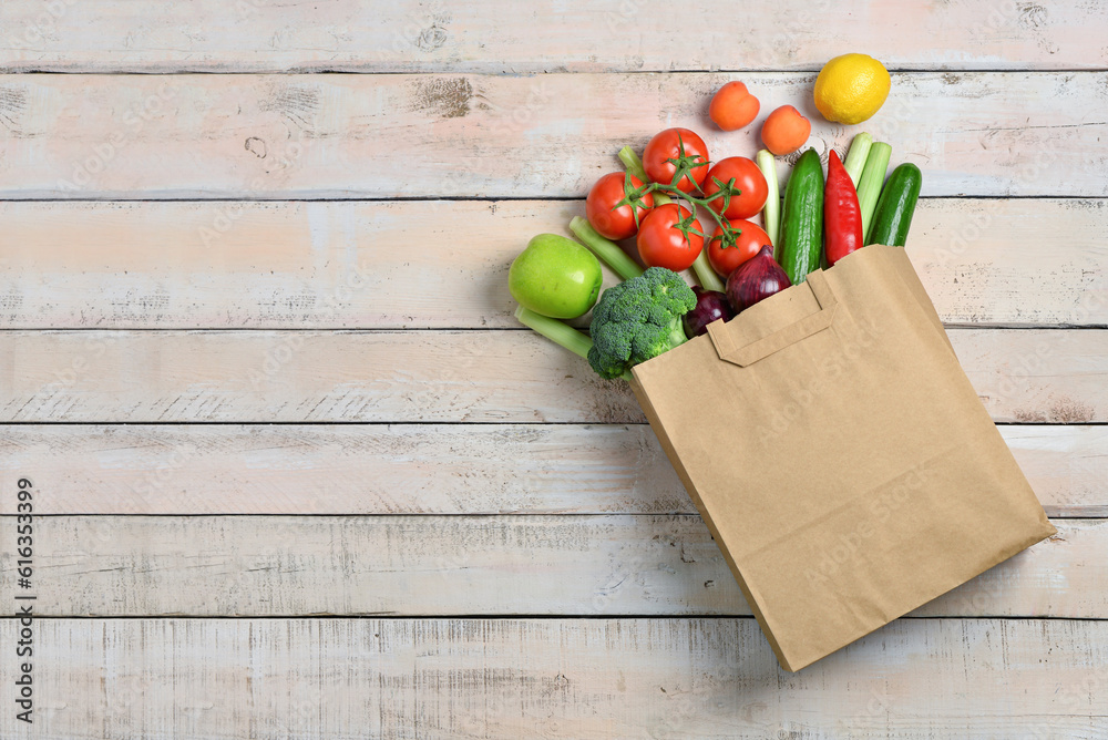 Paper bag with fresh vegetables and fruits on light wooden background