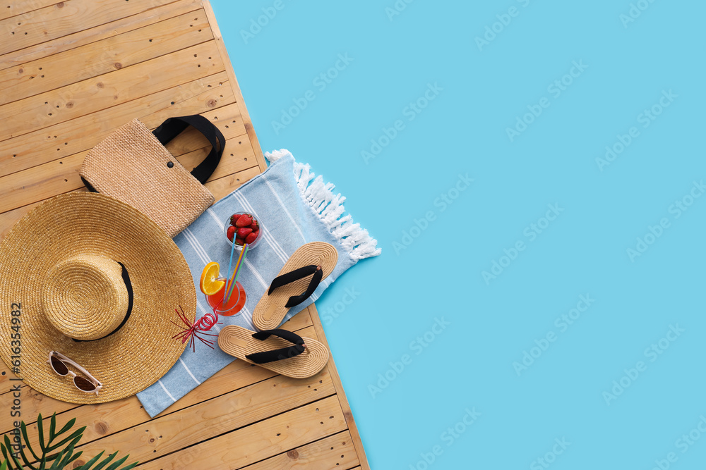 Different beach accessories with bowl of strawberry, cocktail and plant branches on wooden pontoon a