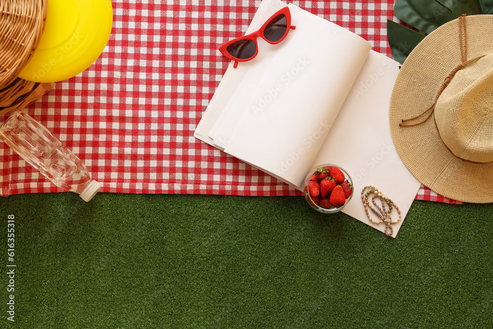 Bowl of fresh strawberry for picnic, empty notebook and beach accessories on red checkered plaid aga