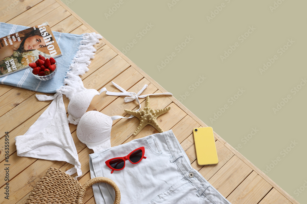 Bowl of strawberry with clothes, beach accessories and mobile phone on wooden pontoon against green 