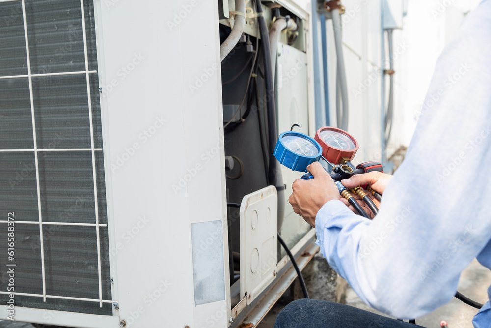 Air repair mechanic using measuring equipment for filling industrial factory air conditioners and ch