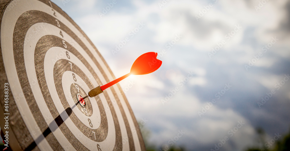 Close up shot red darts arrows in the target  of dartboard center on dark blue sky background. Busin