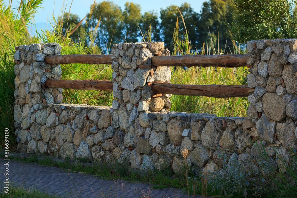 Massive fence with stones and wooden logs. Countryside South Italy details. Evening sunlight with ru