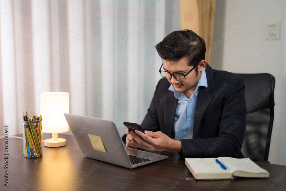 Asian businessman using smart phone on desk with laptop at home.