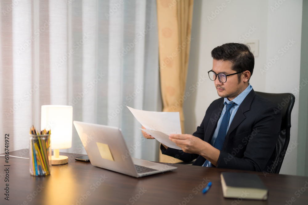 Asian businessman checking inventory on desk with laptop in office.