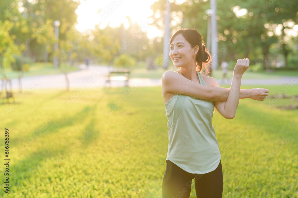 Female jogger. Fit young Asian woman with green sportswear stretching muscle in park before running 