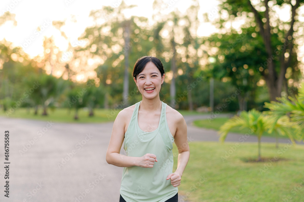 Fit Asian young woman jogging in park smiling happy running and enjoying a healthy outdoor lifestyle