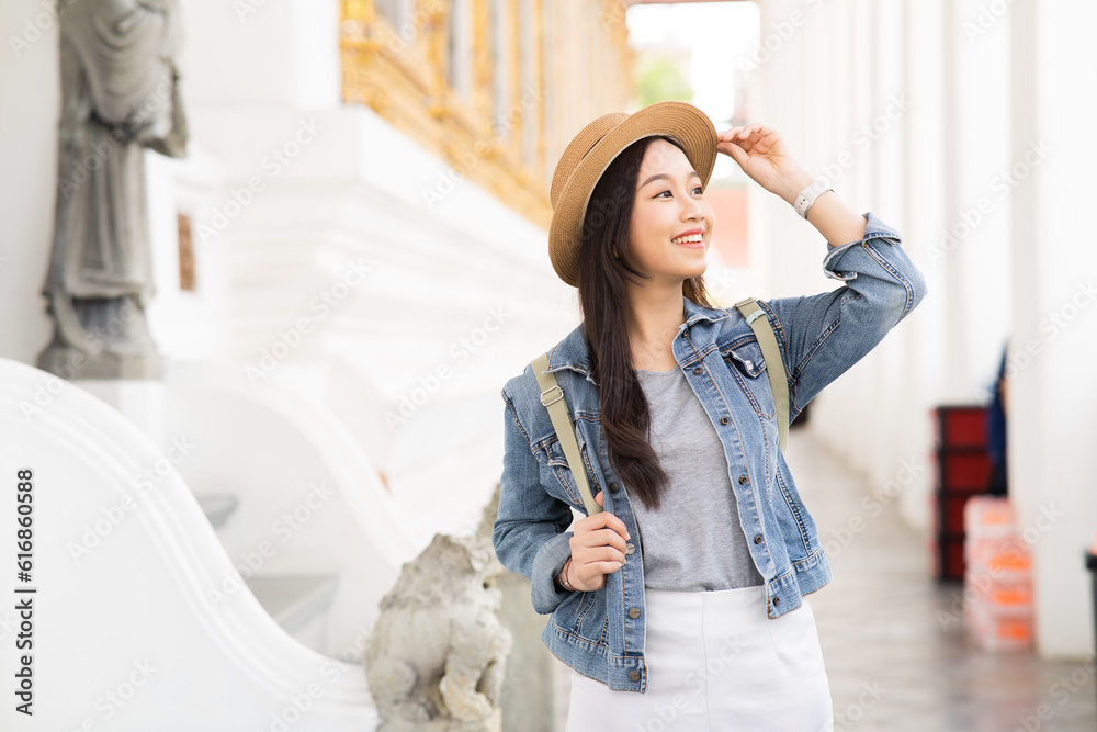 Portrait of Asian female traveler walking on walkway of the temple while smiling back in Bangkok, Th