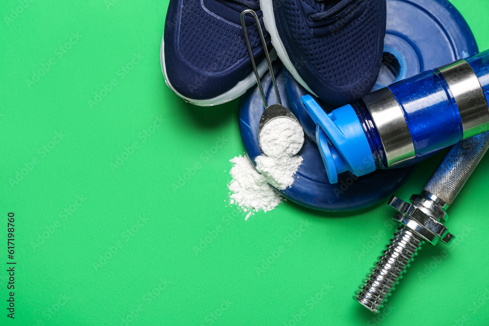 Scoop with amino acid supplement, sports equipment, shoes and bottle of water on green background