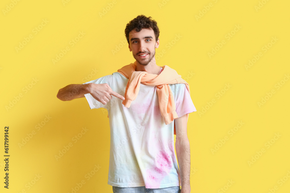 Young man pointing at tie-dye t-shirt on yellow background