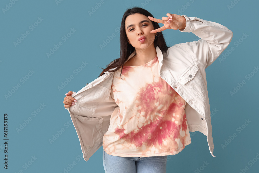 Young woman in tie-dye t-shirt showing victory gesture on blue background