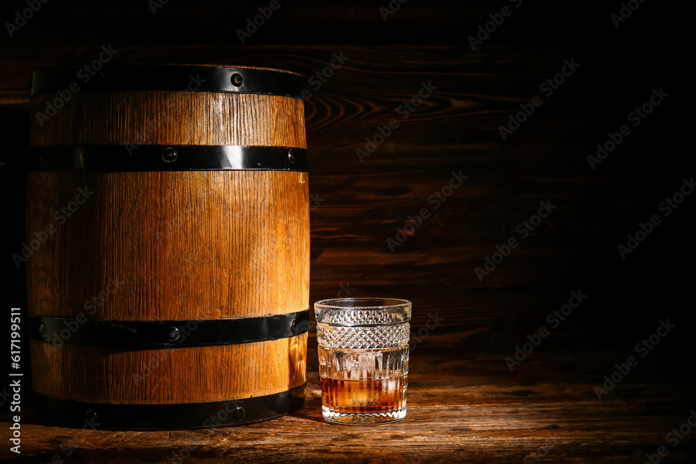 Glass of cold rum and barrel on wooden background